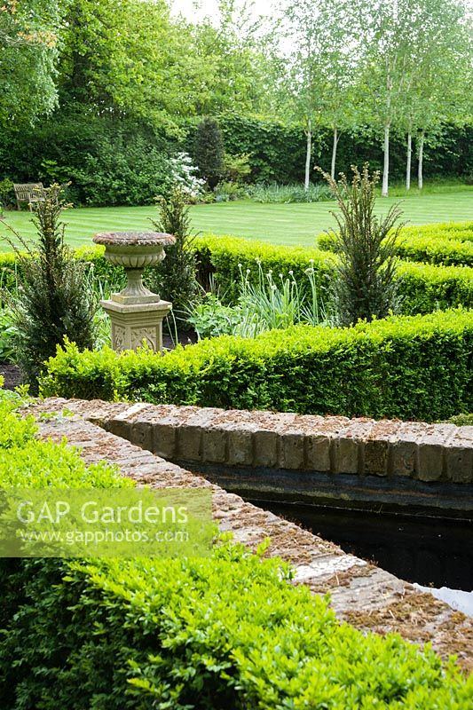 Box edged beds to one side of the house are planted with yews around a central urn.