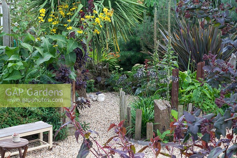 Driftwood, gravel and rusted iron are signature materials in this garden of curving spaces, softened by the textural foliage planting, including Inula magnifica, Cotinus coggrygia, Cordyline, Phormium and Pinus mugo. In the foreground: Physocarpus opulifolius 'Diabolo' and Persicaria microcephala 'Red Dragon'.