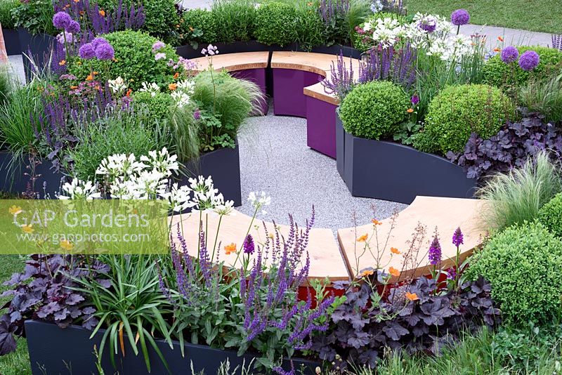 The Urban Connection Garden. Oak Top semi circular seats surrounded by extensive planting in containers. The RHS Chelsea Flower Show 2016, Designer: Lee Bestall Sponsors: Victoria Business Improvement District