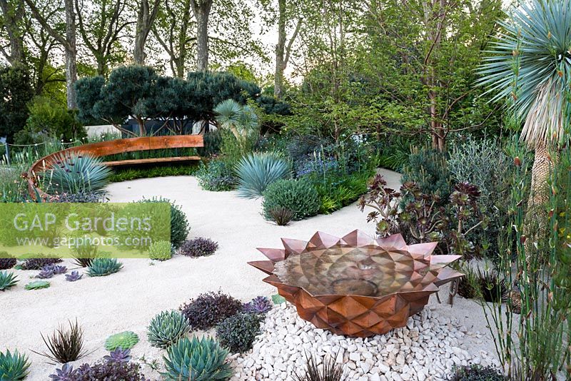 The Winton Beauty of Mathematics Garden, view of copper water feature, curved bench and desert-like sand path surrounded by Yucca rostrata, Dasylirion wheeleri, Pines, Echeveria 'Duchess of Nuremberg', succulents, tropical, Mediterranean plants. The RHS Chelsea Flower Show 2016, Designer: Nick Bailey, Sponsor: Winton