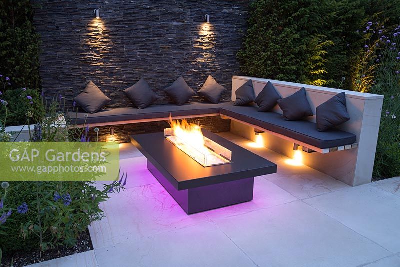 Secluded seating area with a dry stone slate wall and propane fire pit emitting purple light