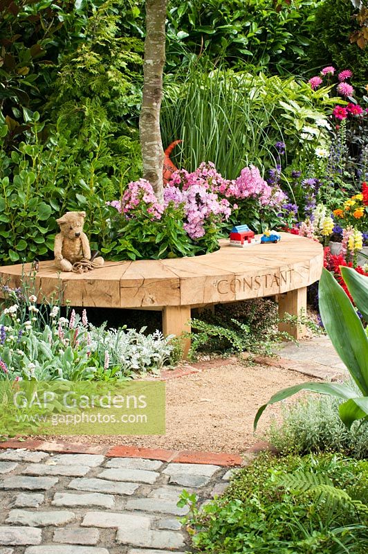 The NSPCC Legacy Garden, Hampton Court Palace Flower Show 2014. Teddy bear and children's toys on wooden bench surrounded by colourful mixed planting