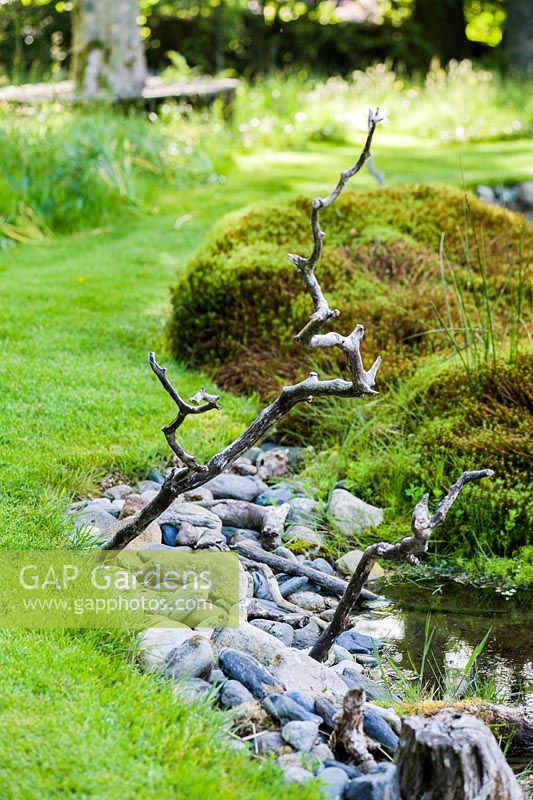 A pair of zig-zag perching sticks are wedged into pebbles beside the still pool.