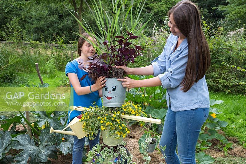 Two girls planting Iresine into the head of the scarecrow