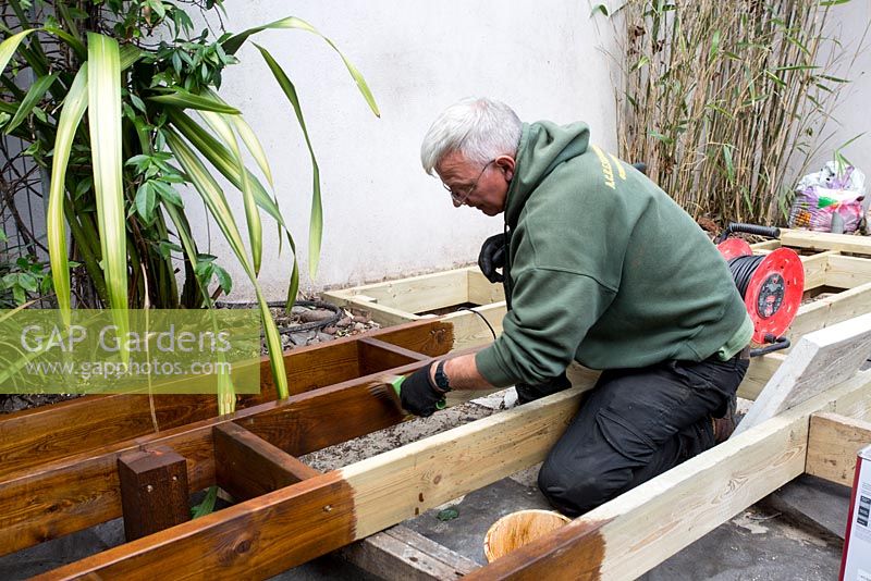Applying wood preservative to joists before laying decking in small urban garden