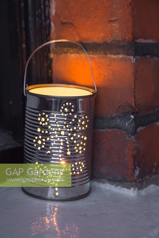 A lit tin can lantern sat on a window ledge
