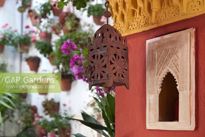 Morrocan style lantern on coloured plaster wall with pelargoniums in background, Cordoba, Spain