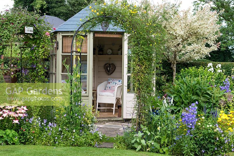 A cottage garden with summer house, clematis covered arch, topiary box and colourful mixed border