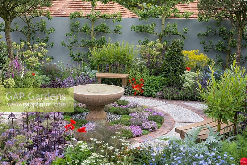 A Modern Apothecary. A courtyard for quiet reflection, planted with medicinal herbs. A circular brick and cobble path encloses a bed of thyme, at its centre a stone water basin created by Karl Friedrich. Designer: Jekka McVicar. RHS Chelsea Flower Show 2016