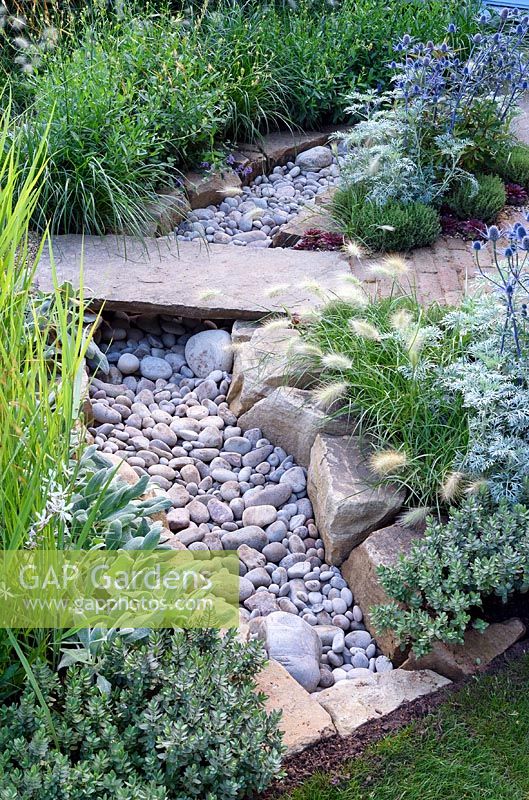 The Drought Garden. Stone bridge over dry stone river in gravelled city garden with drought tolerant planting. Designer: Steve Dimmock. RHS Hampton Court Palace Flower Show 2016