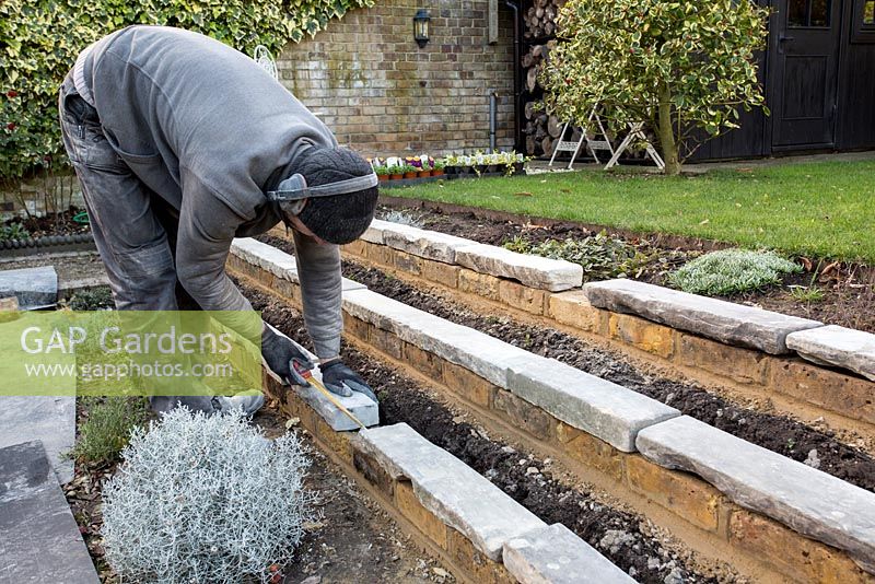 Stepped border in London garden -  landscaper measuring York stone to fit on new brickwork before fixing with cement