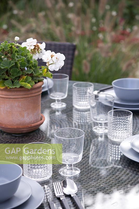 Patio dining table set ready with a potted Pelargonium as the centrepiece