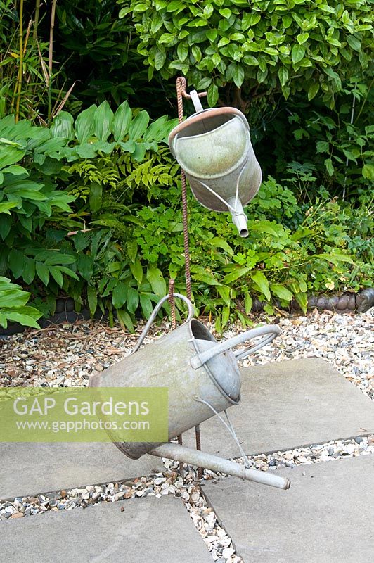 Suspended metal watering cans as a decoration on a patio and mixed border behind