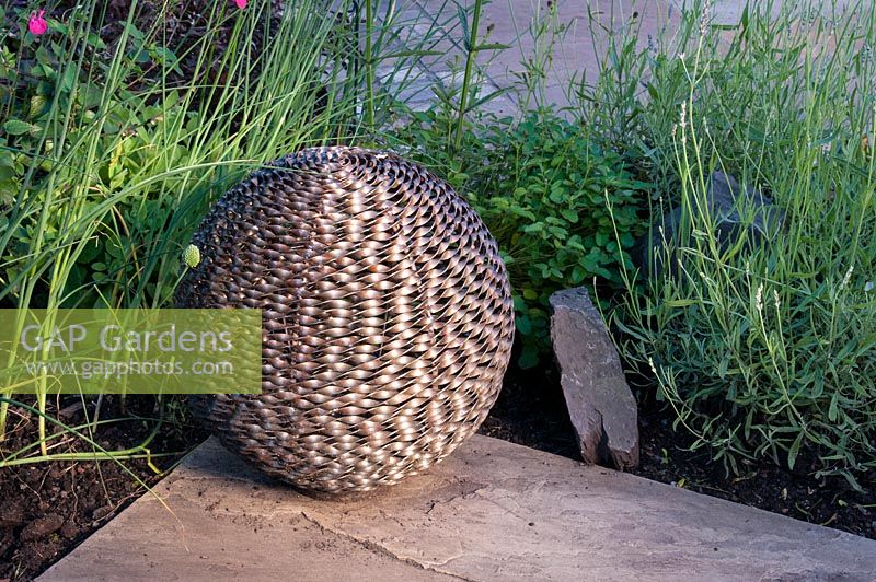 Bronze metal lattice sphere garden feature on paving with adjacent border with Lavandula Salvia and Verbena  