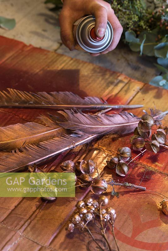 Spray painting goose feathers and rose hips gold