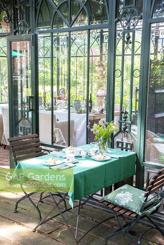 Outside the Art Deco glasshouse, wood and iron garden suite with green tablecloth