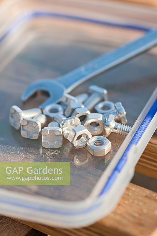 Close up of square headed aluminium bolts, with nuts, used to assemble the glazing bars of aluminium greenhouses. The square head of the bolt slides into the groove of the glazing bar and prevents the bolt from turning when the nut is screwed on and tightened with the spanner: April, Spring.