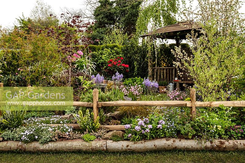 The Water Spout garden - view showing mixed colourful planting, rustic post and rail fencing and sheltered seating area - RHS Malvern Spring Show 2016. Designer: Christian Dowle. Sponsor: Garden Inspiration