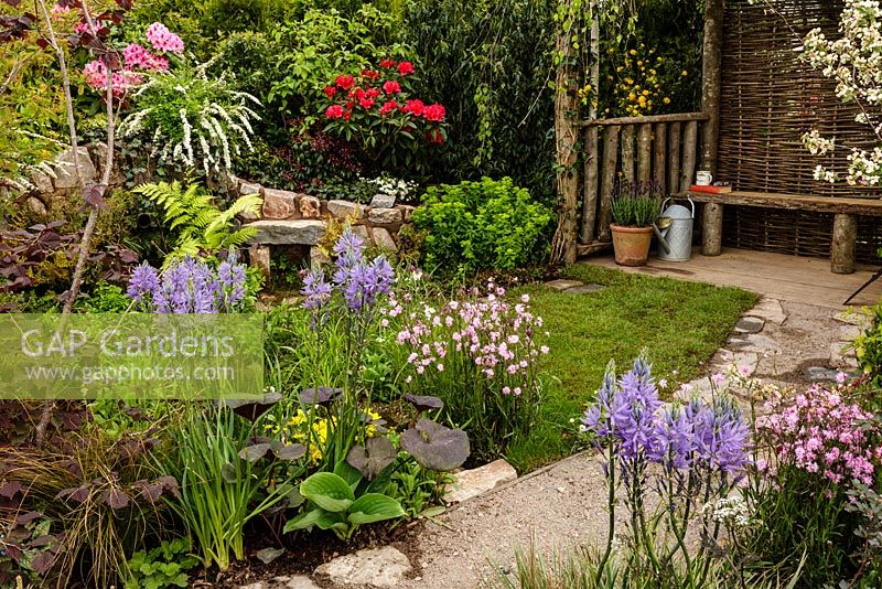 Rustic stone and gravel path leading to seating area through mixed colourful planting including Camassia - Camas lily - The Water Spout garden - RHS Malvern Spring Show 2016. Designer: Christian Dowle. Sponsor: Garden Inspiration
