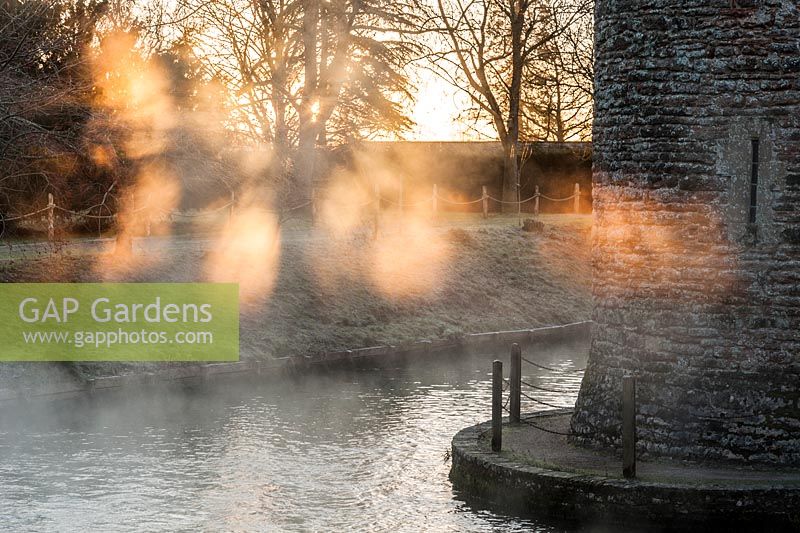 Early morning sun illuminates mist rising from spring water tumbling into the moat around the Bishop's Palace in Wells on a November morning 