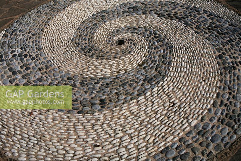 Pebble mosaic made using contrasting white and grey stones on edge to form a whirlpool effect.