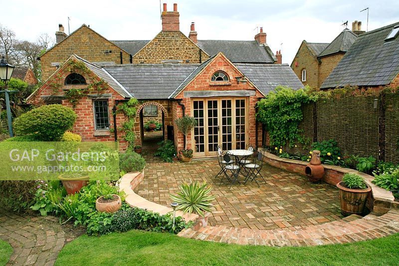 House extension and patio built from recycled materials with a sunken brick patio, steps and curving retaining wall with wrap around planting. 