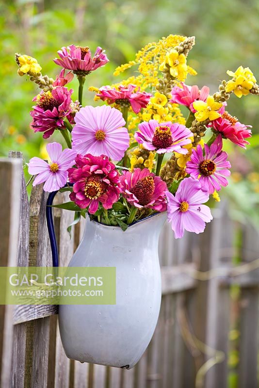 Jug of flowers on te wooden fence. Zinnia, Cosmea, Verbascum and Solidago.