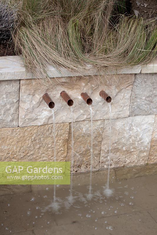 Four copper pipe spigots coming out of a wall with water spilling into a pond