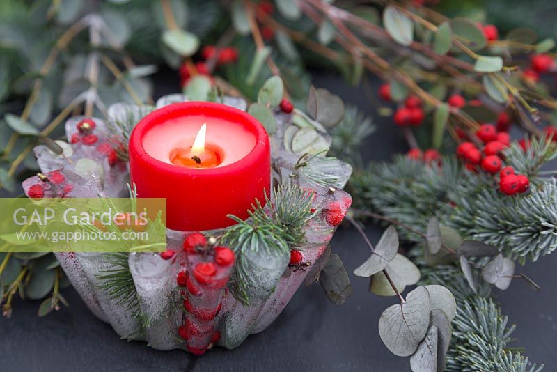 A frozen Jelly mould candle bowl with a lit candle. Constructed from Pine foliage, Eucalyptus and Ilex verticillata berries