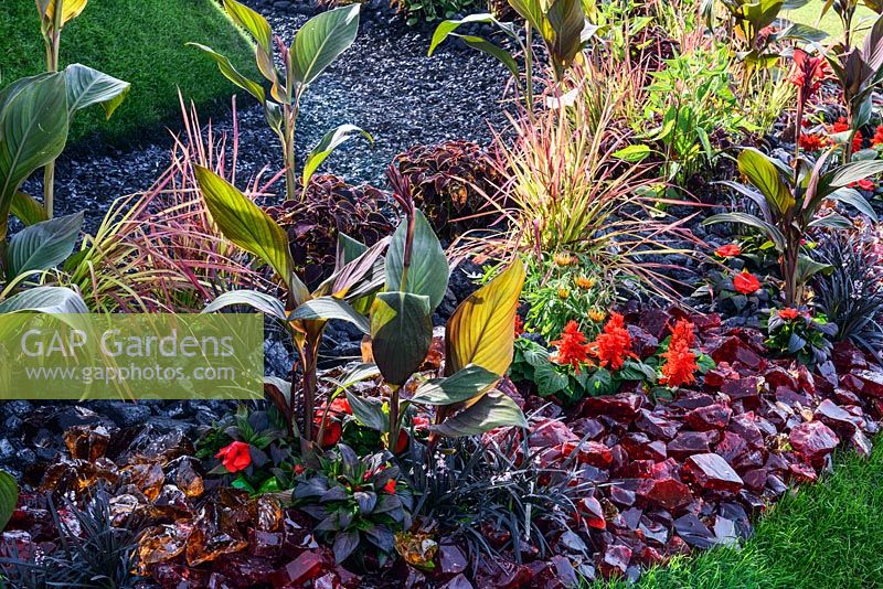 A ring of hot-looking translucent glass rocks and fiery-coloured flowers including dark foliage cannas and coleus. Wormhole Foramen vermis Garden, RHS Hampton Court Palace Flower Show 2016. Designed by John Humphreys, Andy Hyde
