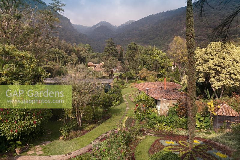 Aerial view of gardens with borders, terracotta roofed houses and tree covered hills beyond - Lake Atitlan Hotel, Guatemala