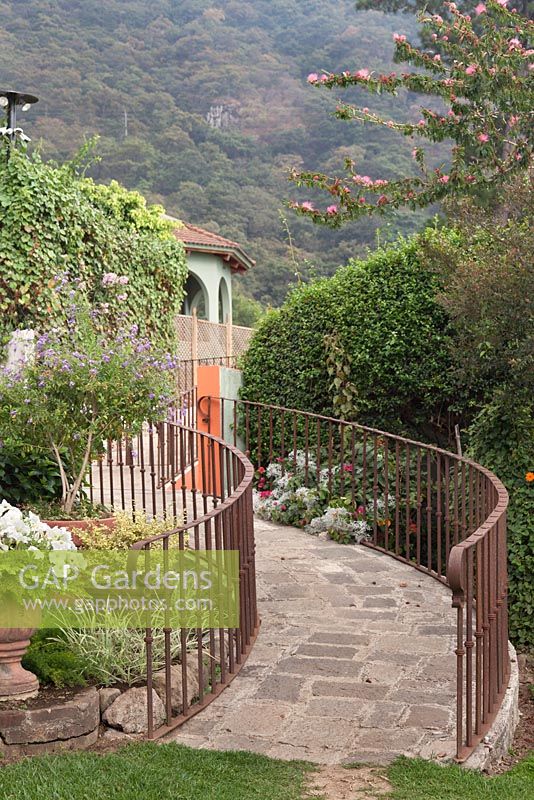 Stone path up curving slope with rusty coloured iron railings in tropical gardens with views to tree covered hills - Lake Atitlan Hotel, Guatemala