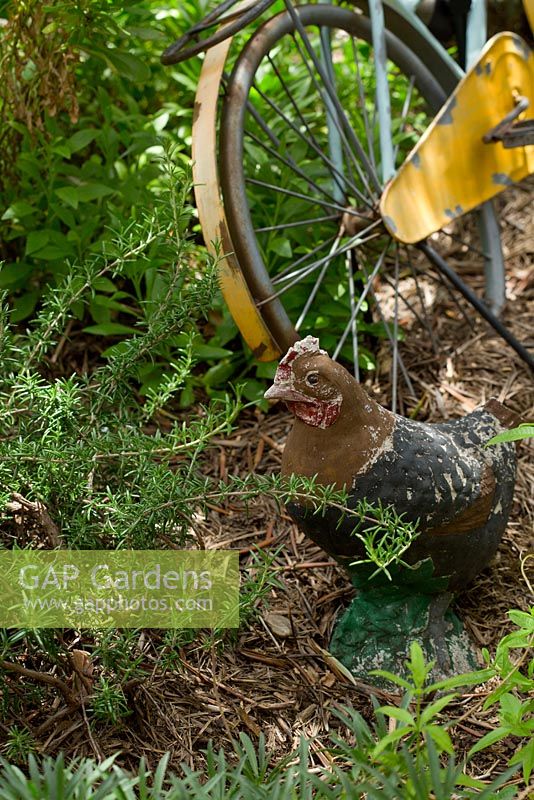 A rustic vintage chicken garden ornament and an old bicycle painted yellow in a herb garden.