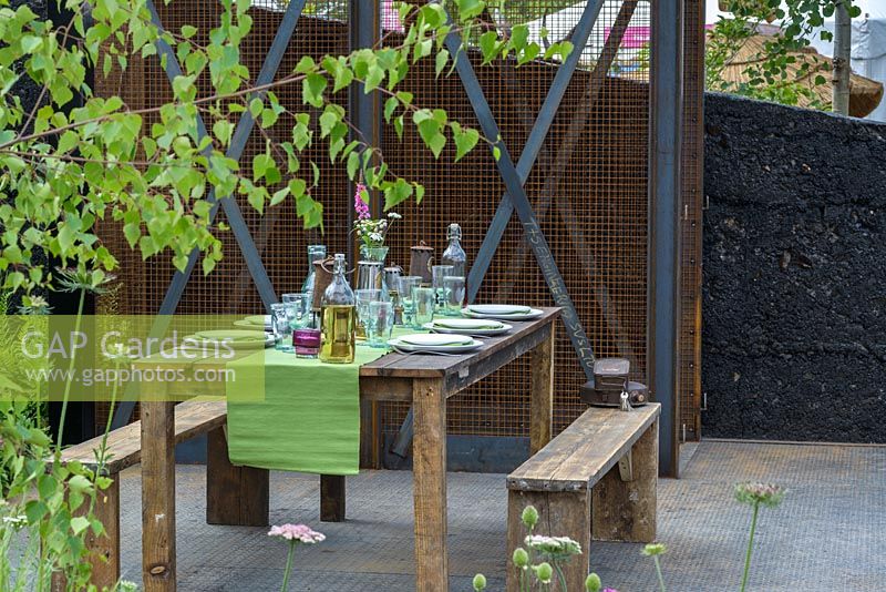 Dining area with wooden table and benches in Green Seam Garden, Hadlow College Facing Change at Hampton Court Flower Show 2015. Design: Stuart Charles Towner, Bethany Williams. Gold - Best In Show