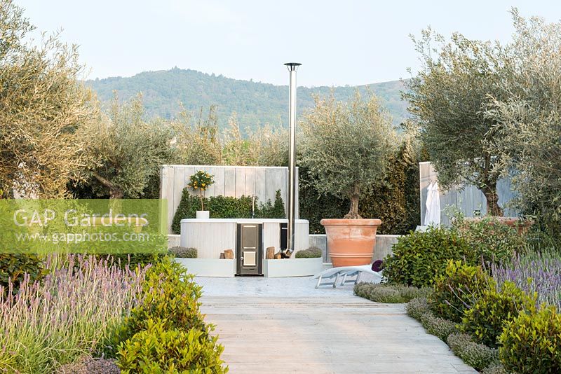 Hot tub fuelled by log burner, Olive trees in terracotta planters, path lined with Prunus lusitanica underplanted with Thymus and Lavandula - The Retreat, RHS Malvern Spring Festival 2017 - Design: Villaggio Verde