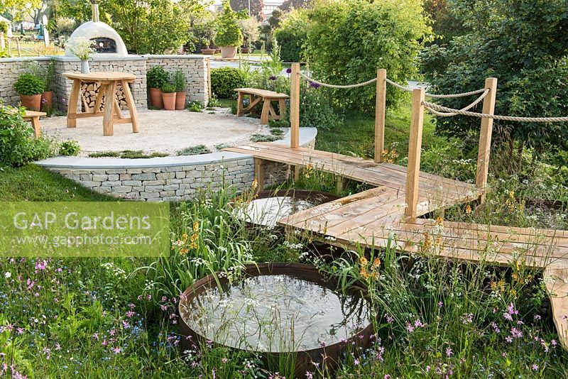 Roped walkway over circular ponds and wildflower meadow, to outdoor pizza oven and seating area - The Refuge Garden in aid of Help Refugees UK, RHS Malvern Spring Festival 2017 - Design: Sue Jollans, Sponsors: Readyhedge, Everedge, Outchester and Ross Farm Cottages