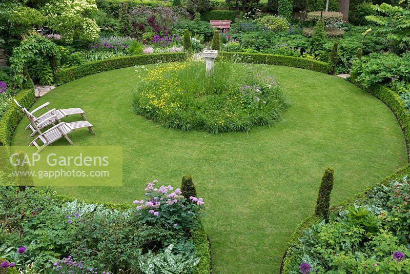 An aerial view of a fifth-of-an-acre cottage garden with circular lawn and raised wildflower mound encircling a bird bath. The formal structure is created by low box hedging with conical shaped yews marking the entrances to multiple paths for exploring the garden.
