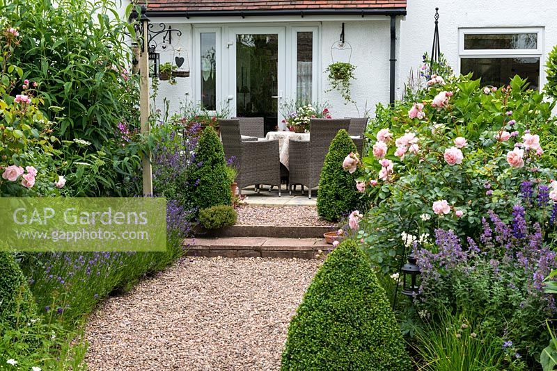 A rising pebble path lined in lavender and roses leads to a terrace with dining table in a sheltered spot outside the sitting room.