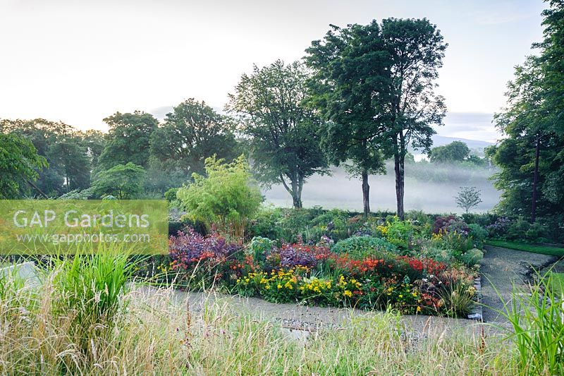 Misty late summer morning at June Blake's garden, viewed from the hillside above colourful beds full