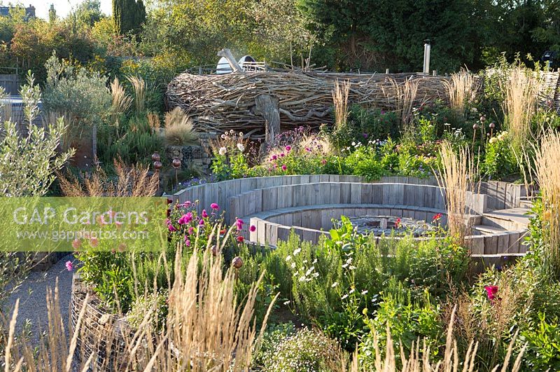 View over mixed borders of pub garden with willow fence and wooden seating. Jo Thompson garden Design, Ticehurst, East Sussex