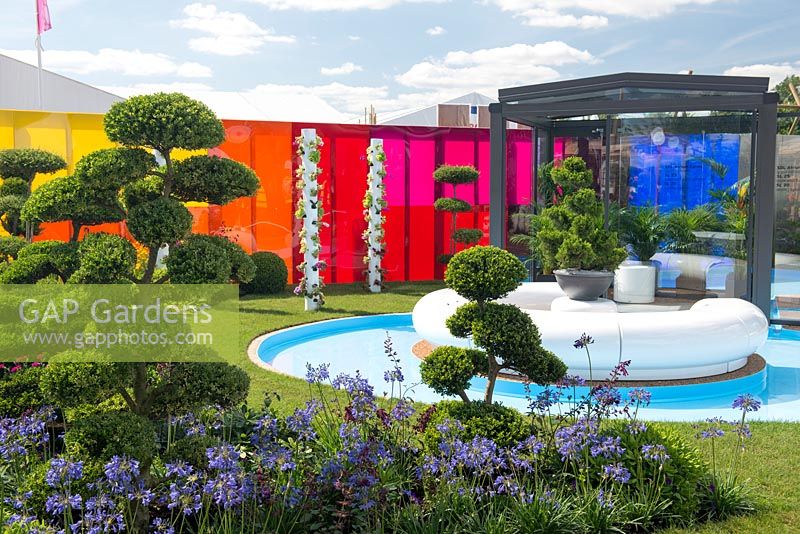 Cloud topiary, Buxus sempervirens underplanted with Agapanthus and Salvia, GRP seating surrounded by a circular rill, hydroponic salad towers, with a backdrop of coloured acrylic panelling - Journey of Life, RHS Hampton Court Palace Flower Show 2017