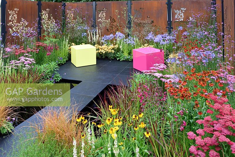 Colour Box garden. Rusty metal fence panels with laser cut floral patterns with red, pink and blue planted borders. Designers: Charlie Bloom and Simon Webster. RHS Hampton Court Palace Flower Show 2017