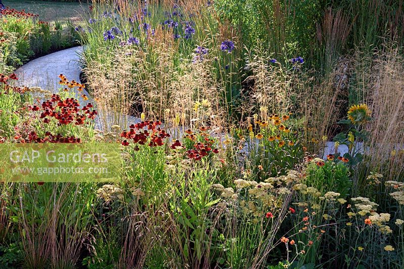 The Perennial Sanctuary Garden. Reds and Yellows in Spiralling borders. Helenium, Achillea, Kniphofia and grasses. Designer: Tom Massey. RHS Hampton Court Palace Flower Show 2017


