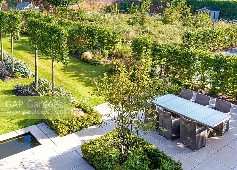 Long herbaceous borders lead to a patio area with a rill and seating, designed by Louise Harrison-Holland. Plants include Amelanchier lamarckii, box hedging, pleached Pyrus calleryana 'Chanticleer', Japanese anemones, Stachys, Persicaria, Ophiopogon planiscapus 'Nigrescens', and Miscanthus sinensis 'Kleine Fontaine'

