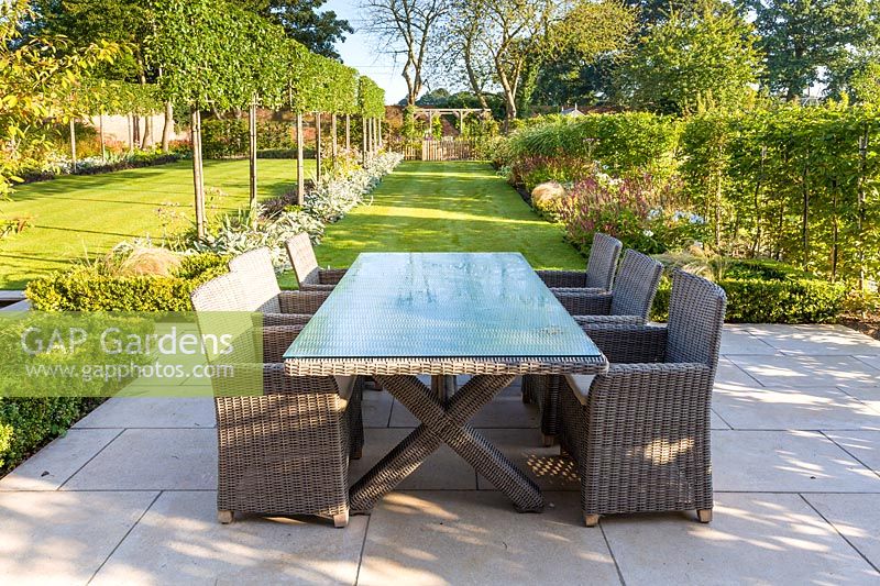 Seats and a table on a large patio, designed by Louise Harrison-Holland. Plants include pleached Pyrus calleryana 'Chanticleer', Japanese anemones, Stachys, Persicaria, Ophiopogon planiscapus 'Nigrescens' and Miscanthus sinensis 'Kleine Fontaine'. 