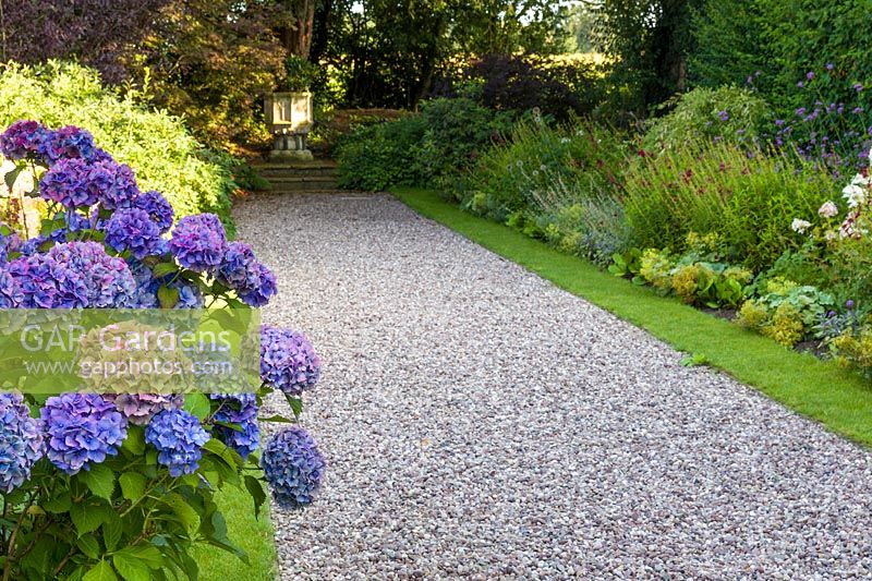 An ancient font provides a focal point in a newly renovated double herbaceous border in a modern Cheshire country garden, designed by Louise Harrison-Holland. Planting includes Phlox paniculata, Verbena bonarienses and Hydrangea macrophylla