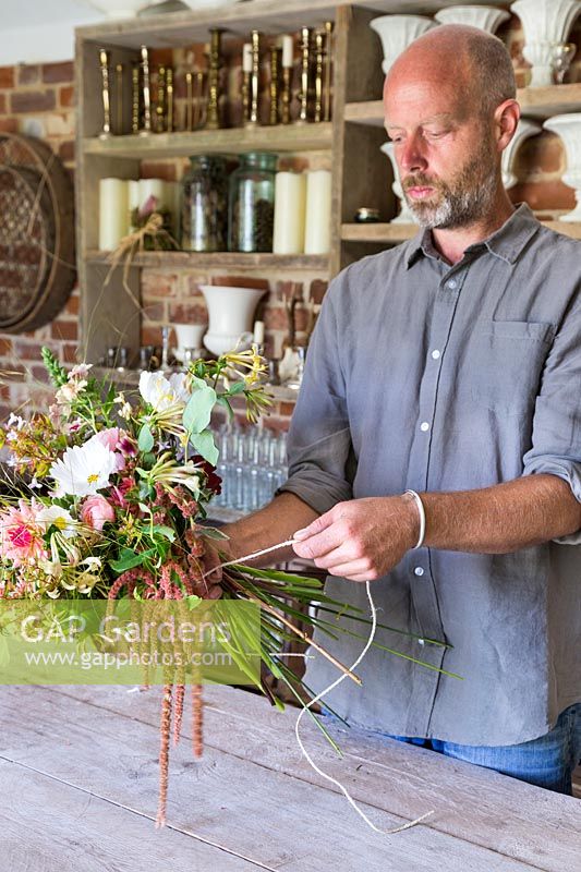Man tying a bouquet with Dahlias, Rosa, Digitalis and foliage