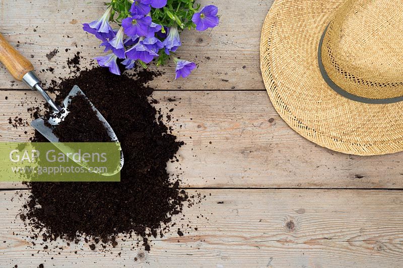 Summer hat and compost with trowel on wooden surface