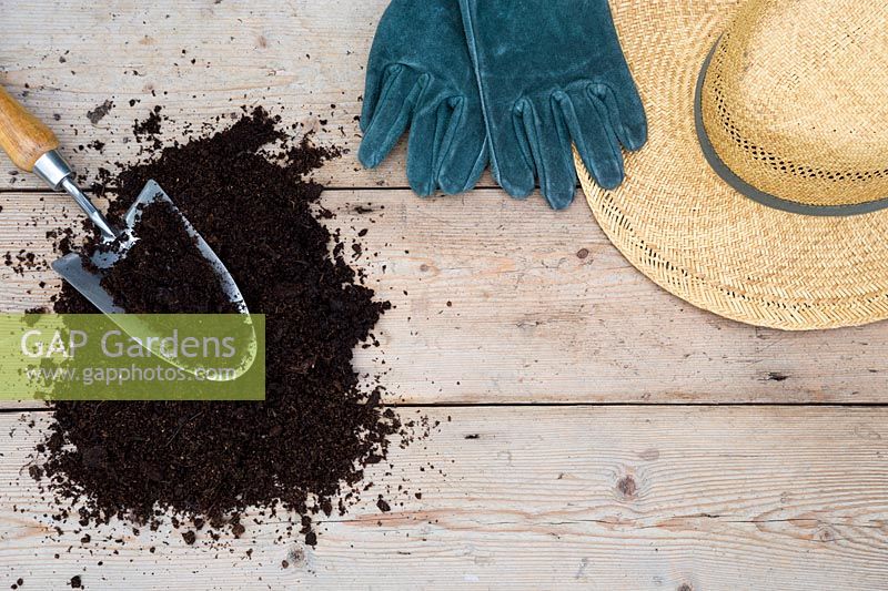 Summer hat, gardening gloves and compost with trowel on wooden surface