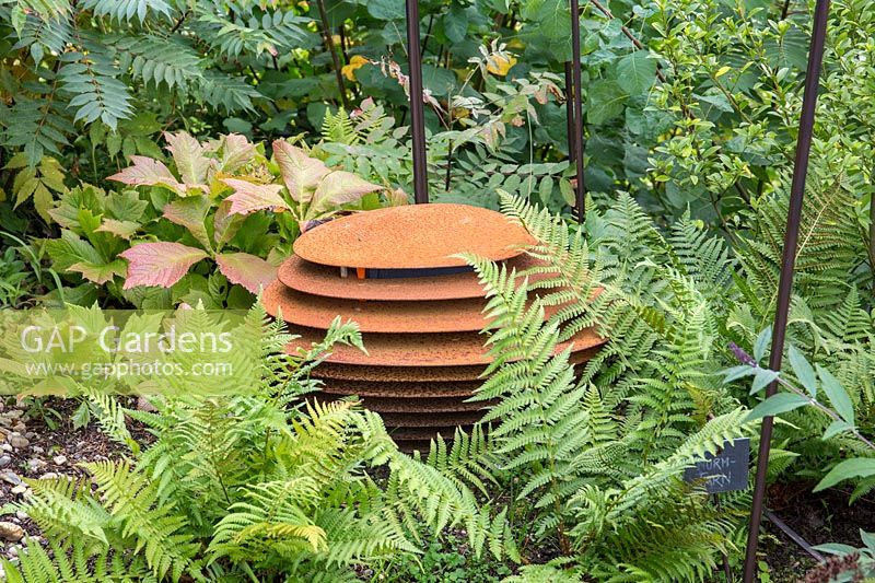 Rusty iron loudspeaker box in shady planting with ferns